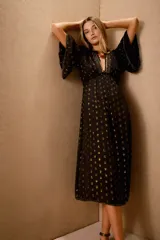 Vestido midi negro con lunares dorados, escote en V, mangas anchas al codo con bordado de lentejuelas y mostacillas. Corte amplio con ajuste elástico en la cintura y forro de algodón.