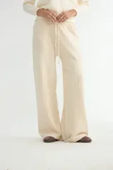 Pantalón de punto color crema, de corte recto y holgado, con cintura elástica y cordón ajustable. Presenta costuras verticales decorativas a lo largo de las piernas.