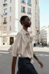 Camisa de cuello solapa y manga corta, con diseño a rayas verticales. Presenta cierre frontal con botones y detalle de lazada en el bajo delantero.