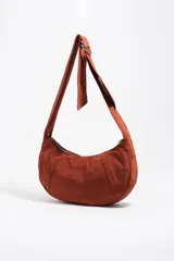Bolso tipo hobo de la marca Bimba y Lola, modelo Moon mediano, de color rojo óxido. Confeccionado en nylon con diseño de media luna, cierre superior con cremallera, correa ajustable con hebilla metálica y el logotipo de la marca impreso en la parte frontal.