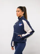 Campera deportiva Umbro del Club Nacional de Football, con diseño de bloques de color en azul marino y blanco. Presenta cuello alto, cierre frontal completo, bolsillos laterales y el escudo del club junto al logo de la marca en el pecho.