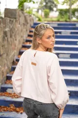 Blusa color rosa pálido de lino con lurex, escote redondo con detalle de nido de abeja, mangas largas con puños elásticos y cierre trasero con botón.