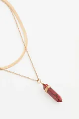 Collar doble de metal dorado compuesto por una cadena tipo serpiente y una cadena fina con dije de piedra sintética roja en forma de punta envuelta en alambre.