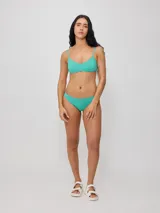 Top de bikini con tirantes finos y escote redondo, confeccionado en poliamida con elastano, con estampado tropical en tonos verdes, celestes y salmón sobre fondo negro.