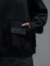 Hoodie oversize color negro, confeccionado en frisa gamuzada de algodón con recortes en hombros y bolsillo frontal tipo cargo con solapa en material técnico. Presenta capucha forrada y puños y ruedo acanalados.