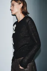 Chaqueta de punto negra con cuello redondo y manga larga. Presenta bordados florales en color blanco en la parte delantera y cierre frontal con botones.