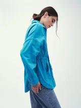 Chaqueta color beige con cuello camisero, cierre frontal con botones, cintura ajustable con cordón y cuatro bolsillos frontales.