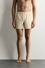 Short de baño de tejido técnico en color beige con estampado paisley en tonos claros y naranjas. Cuenta con cintura elástica con cordón ajustable, bolsillos laterales y forro interior.