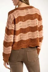 Sweater de tejido de punto con diseño de rayas horizontales onduladas en tonos marrón y beige. Presenta cuello redondo, mangas largas y corte oversize.