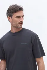 Remera de manga corta color gris oscuro con cuello redondo y calce regular. Presenta un estampado artístico rectangular en la espalda con diseño de manchas en tonos azules y texto descriptivo.