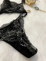 Conjunto de lencería compuesto por bralette triangular y tanga, confeccionado en encaje bitono negro y blanco. El bralette presenta cierre frontal con broche de gancho y breteles regulables. La tanga es de estilo colaless con laterales regulables mediante herrajes metálicos.
