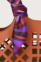 Pañuelo cuadrado de acabado sedoso con estampado que combina motivos florales en tonos violetas y patrones geométricos en marrón y bordó. Presenta el logo de la marca estampado en los bordes.