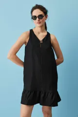 Vestido corto de lino color beige, de silueta suelta y sin mangas, con escote en V decorado con un botón, bolsillos laterales y detalle de volado en el ruedo.