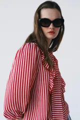 Camisa de manga larga con estampado de rayas rojas y blancas, cuello con lazo, volantes frontales y cierre de botones.