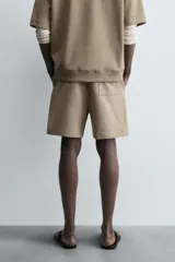 Bermuda de algodón color beige claro, corte relajado (relaxed fit), con cintura elástica ajustable mediante cordón y bolsillos laterales y trasero de plastrón.