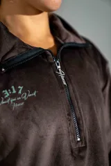Buzo de plush color marrón, con cuello alto y cierre frontal parcial. Presenta un diseño holgado con puños elásticos y un pequeño bordado en el pecho.