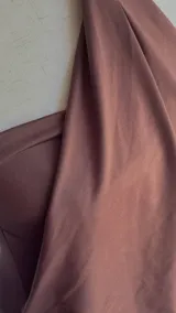 Vestido corto color marrón con diseño de cuello halter, caracterizado por un detalle de argolla circular en el centro del escote y una caída fluida y drapeada en la parte superior, contrastando con una falda ajustada.