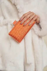 Clutch rígido color naranja, completamente cubierto de tachas brillantes del mismo color. Tiene un cierre metálico plateado y una correa corta de tela naranja.