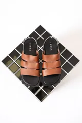 Sandalias chatas color marrón con tiras anchas de cuero y pulsera al tobillo con hebilla metálica.