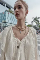 Pack de tres collares superpuestos de metal en tonos dorado y plateado. El collar más corto tiene un dije colgante en forma de reloj ovalado con piedras de colores. El collar intermedio tiene un dije colgante en forma de reloj redondo con marco floral. El collar más largo consiste en múltiples cadenas finas, algunas con cuentas, y un dije colgante en forma de estrella de múltiples puntas.