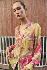 Blusa de manga larga con estampado floral en tonos rosados, verdes y beige. Presenta escote en pico con detalle de abalorios colgantes y cierre frontal con botones.