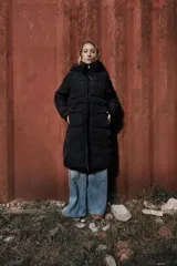 Campera larga acolchonada de corte midi, con capucha amplia, cierre frontal con cremallera y broches a presión, y bolsillos delanteros de gran tamaño con tapa.