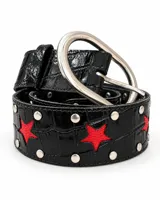 Cinturón de cuero sintético negro con textura símil cocodrilo, detalles de tachas metálicas plateadas y apliques de estrellas rojas. Cuenta con hebilla metálica ovalada grande.