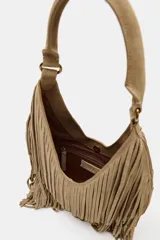 Bolso de hombro tipo shopper confeccionado en serraje, con diseño de doble capa de flecos largos en el cuerpo. Cuenta con asa de hombro integrada, cierre mediante botón imantado y bolsillo interior con cremallera.