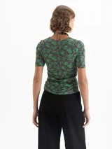 Top de punto color verde con estampado de dragones en tonos marrones y violetas. Tiene escote redondo, mangas cortas y frunces laterales que realzan la silueta.
