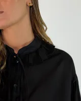 Camisa negra de corte holgado con cuello tipo bebé con volados y lazo de ajuste, cierre frontal con botones y mangas largas abullonadas con puños abotonados.