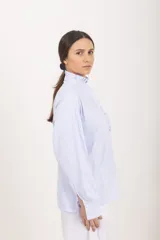Camisa de manga larga a rayas celestes y blancas, con cuello alto mao y volados frontales a lo largo de la botonadura.