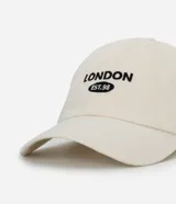 Gorra de sarga color beige claro con visera curva y bordado frontal en negro que dice "LONDON EST.98". Es ajustable en la parte trasera.