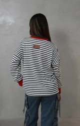 Sweater de punto con diseño a rayas horizontales en blanco y negro, cuello redondo y puños en color rojo vibrante. Presenta un calce relajado y holgado.