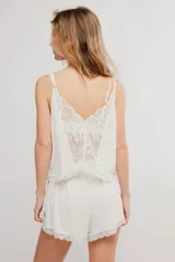 Conjunto de dos piezas de color blanco, confeccionado en viscosa fluida y liviana. Incluye una musculosa con escote en V, detalles de encaje y tirantes finos regulables, y un short con cintura elastizada y bordes de puntilla.