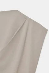 Top de algodón color beige con cuello recto, mangas asimétricas y detalle de tejido drapeado en el frente.