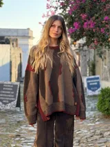 Sweater de tejido de punto con diseño de rayas verticales irregulares en tonos marrones y detalles en color bordó. Presenta cuello redondo, mangas largas y aberturas laterales en el ruedo.