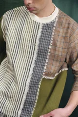 Buzo de manga larga con diseño patchwork que combina diferentes texturas y estampados, incluyendo tejido waffle verde oliva, tejido a rayas y cuadros en tonos grises y marrones, unidos con costuras visibles.