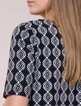 Remera de algodón con estampado geométrico en blanco y negro, de manga corta, con detalle de guarda roja y flecos en el ruedo.