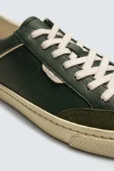 Zapatilla deportiva de estilo retro con diseño de paneles en cuero sintético color verde oscuro, detalles en crema y suela de goma en contraste.