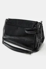 Bolso de hombro con solapa, confeccionado en material sintético con acabado brillante y efecto envejecido. Presenta un diseño estructurado con costuras decorativas, tres compartimentos internos, uno de ellos con cierre de cremallera, y asa de cadena metálica. Se cierra mediante un imán oculto.
