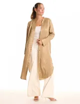 Túnica satinada color dorado con estampado animal print, de silueta oversize y fluida, largo maxi. Cuello a la base con abertura central y botones a tono. Manga larga de corte recto con puños amplios y cierre de botones. Espalda con canesú horizontal recto del cual nace un tablón central profundo. Bajo asimétrico redondeado con tajos laterales profundos, el largo de espalda mayor al largo delantero.