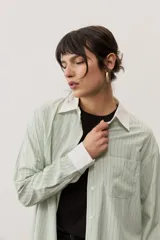 Camisa oversize a rayas color verde menta con cuello y puños en contraste de color blanco. Presenta cierre frontal con botones y un bolsillo aplicado en el pecho.