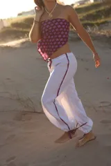 Pantalon de lino color blanco, de corte holgado y estilo babucha, con detalles de franjas estampadas en los laterales y cordones ajustables en los tobillos.