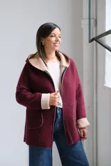 Tapado de paño bordó con interior en color beige, diseño con capucha, cierre frontal y bolsillos laterales. Presenta costuras visibles y puños vueltos que dejan ver el contraste de color.