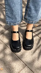 Guillerminas Mathi de color negro, con plataforma robusta, suela dentada y pespuntes blancos. Tienen una tira en el empeine con hebilla metálica y combinación de texturas.