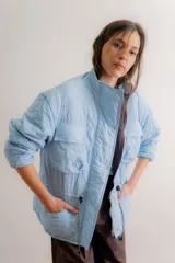 Campera parka reversible de diseño capitoneado con patrón de flores, color celeste. Presenta cuello alto, cierre frontal con botones a presión, bolsillos frontales tipo cargo y cordón ajustable en la cintura.