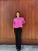 Camisa fucsia de tela con perforaciones tipo broderie, de corte holgado, cuello redondo con pequeña abertura en V, cierre frontal con botones y mangas tres cuartos con puños elásticos.