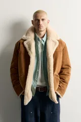 Campera marrón de piel con interior de borreguillo color crudo, de corte regular fit, con cuello bowling, bolsillos de doble vivo y cierre frontal con botones.
