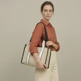 Bolso tipo tote en lona beige con detalles en negro y tiras de hombro blancas y negras. Cuenta con correa ajustable y desmontable.