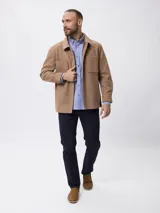 Sobrecamisa de paño color beige, con cuello clásico, cierre frontal con botones metálicos y bolsillos frontales. Presenta un diseño de corte recto y aberturas laterales en el ruedo.